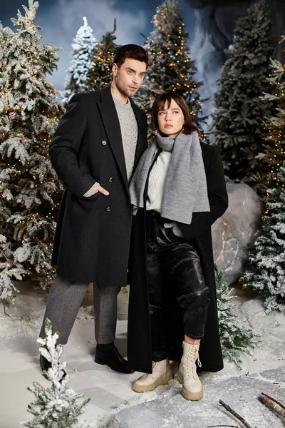 Couple embraces the festive spirit, surrounded by snow-covered pine trees during the holiday season. — Stock Photo