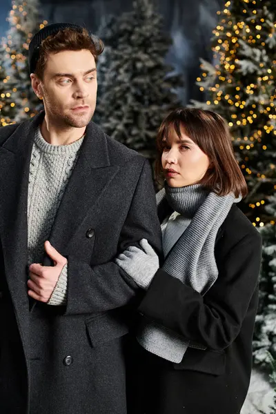 A couple dressed in winter coats shares a warm moment near snow-covered pine trees during the festive season. — Stock Photo