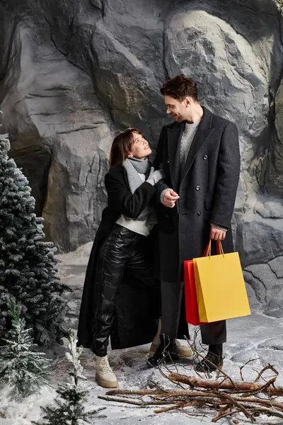 A happy couple shares a special moment in winter coats, surrounded by snowy pines and festive cheer. — Stock Photo