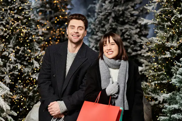 A cheerful couple dons winter coats as they enjoy a festive moment amid snowy pine trees, spreading holiday cheer. — Stock Photo
