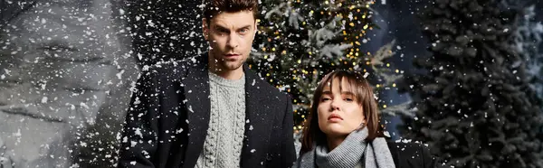 A beautiful couple enjoys the festive atmosphere in winter coats surrounded by snow-covered pine trees. — Stock Photo