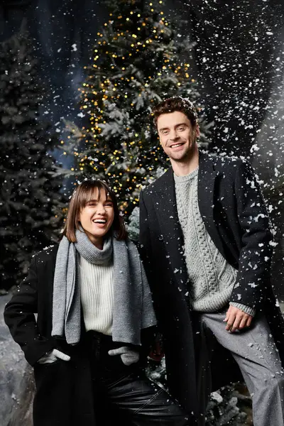 A loving couple smiles warmly together surrounded by snow-covered pine trees, capturing festive cheer. — Stock Photo