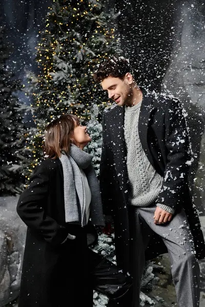 A beautiful couple shares a warm moment surrounded by snow and pine trees, wishing everyone joy and cheer. — Stock Photo
