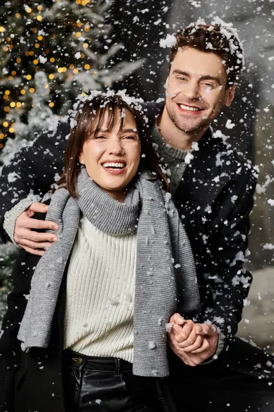 A couple celebrates the festive season, laughing joyfully amidst snow-laden pine trees on a winter day. — Stock Photo