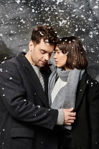 A couple in winter coats shares a tender moment under falling snow, celebrating love. — Stock Photo