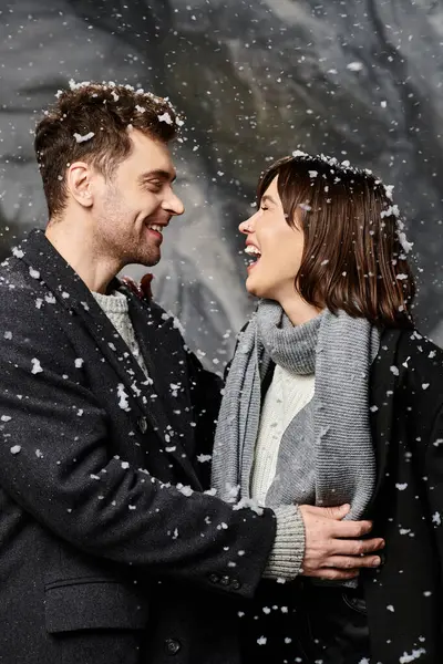 Una coppia amorevole si abbraccia gioiosamente mentre la neve cade intorno a loro, celebrando insieme la stagione invernale. — Foto stock