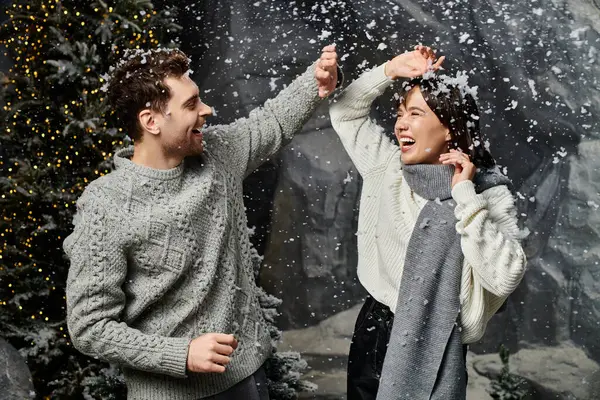 A happy couple laughs together, enjoying snowflakes as they celebrate the festive season among snowy trees. — Stock Photo