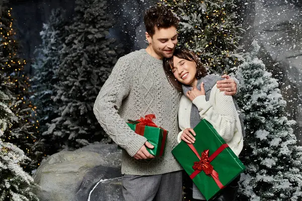 A happy couple embraces warmly near snow-covered fir trees, celebrating the holiday spirit together. — Stock Photo
