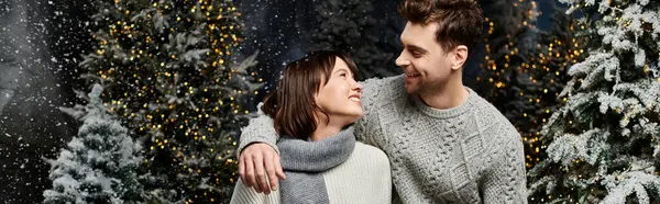 A joyful couple in cozy sweaters smiles by snow-covered fir trees, celebrating Christmas and New Years cheer. — Stock Photo
