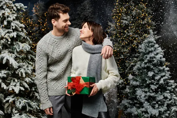 A lovely couple smiles at each other near snow-covered trees, celebrating Christmas with warmth and joy. — Stock Photo