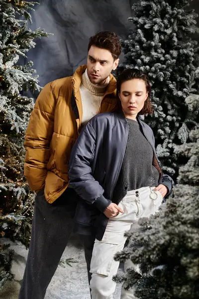 A warm-hearted couple embraces the festive spirit, surrounded by snow-laden pine trees on a winter day. — Stock Photo