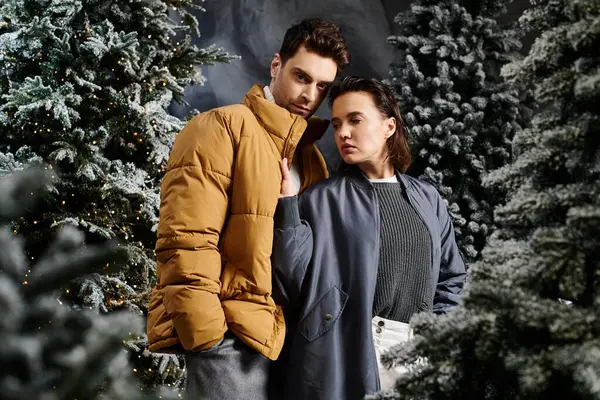 A beautiful couple embraces in warm winter jackets, standing among snow-covered pine trees celebrating Christmas. — Stock Photo