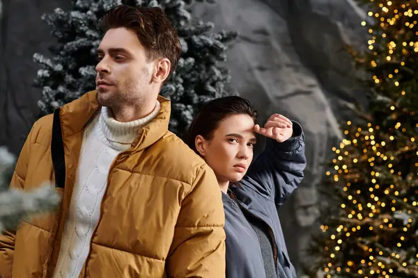 A couple dressed in cozy jackets stands near snow-dusted pines, enjoying a festive winter moment together. — Stock Photo