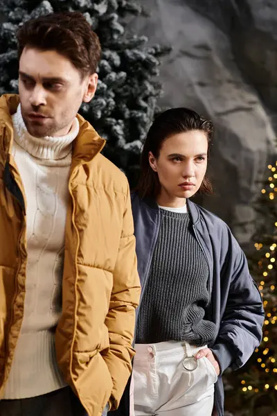 A stylish couple dressed warmly stands close together amid snow-covered pine trees, spreading holiday cheer. — Stock Photo