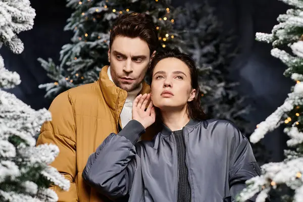 A beautiful couple stands closely together, exuding warmth and love near snow-covered pine trees. — Stock Photo