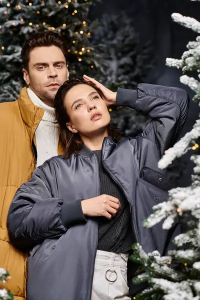 A beautiful couple embraces the holiday spirit in warm jackets amid snow-laden pine trees. — Stock Photo