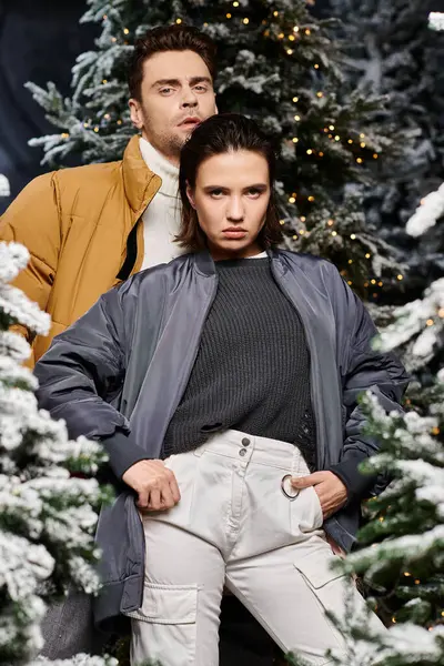 A fashionable couple stands confidently near snow-covered pine trees, embracing the festive Christmas spirit. — Stock Photo