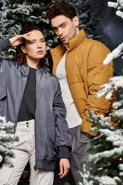 A couple embraces the winter spirit, dressed warmly, surrounded by snow-covered pine trees. — Stock Photo