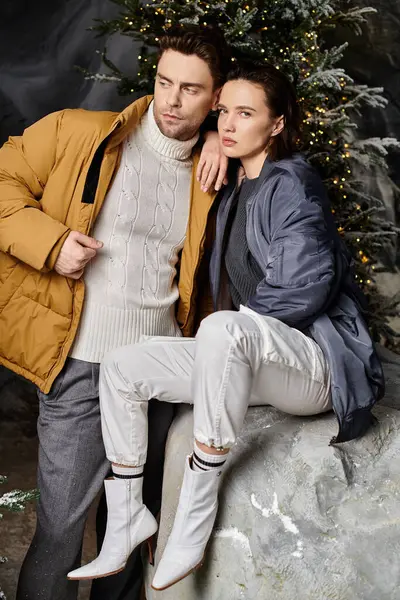 A couple in warm winter jackets shares a tender moment near snow-covered pine trees, embracing the holiday spirit. — Stock Photo