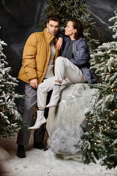 A couple dressed in warm jackets enjoys a festive moment surrounded by snow-covered pine trees. — Stock Photo