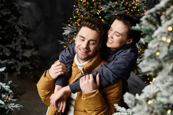 A couple in warm winter jackets shares a joyful moment near snow-draped pine trees, radiating holiday cheer. — Stock Photo