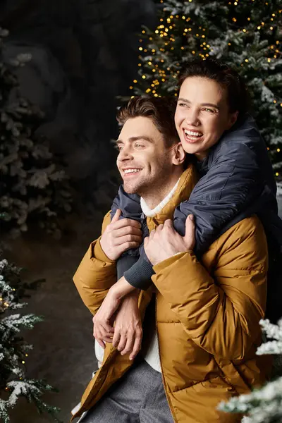 A happy couple in cozy jackets shares a warm moment amidst snow-covered pine trees celebrating Christmas. — Stock Photo
