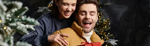 A loving couple shares a moment near snow-covered pine trees, exchanging gifts and holiday cheer. — Stock Photo