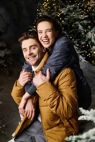 A cheerful couple shares a warm embrace amid snow-covered pine trees, celebrating the spirit of Christmas. — Stock Photo