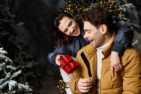 A couple bundled in stylish winter jackets shares a joyful moment, exchanging Christmas gifts surrounded by snow. — Stock Photo