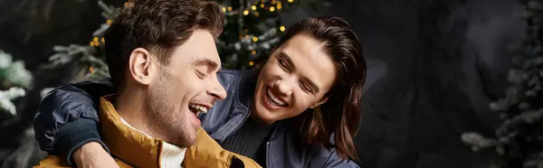 A joyful couple laughs in cozy winter jackets amid snow-covered pines, celebrating Christmas. — Stock Photo