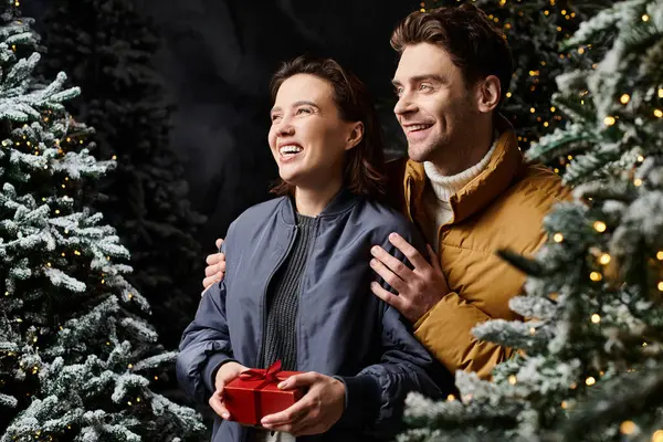 A warmhearted couple smiles amidst snow-covered pine trees, sharing the magic of Christmas together. — Stock Photo