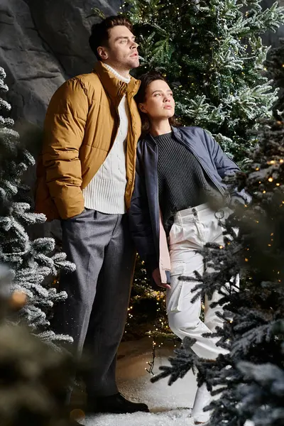 A couple enjoys a romantic moment in warm jackets while surrounded by snowy pine trees and holiday spirit. — Stock Photo