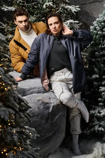 Una pareja disfruta del espíritu festivo en cálidas chaquetas de invierno rodeadas de hermosos pinos cubiertos de nieve.. - foto de stock