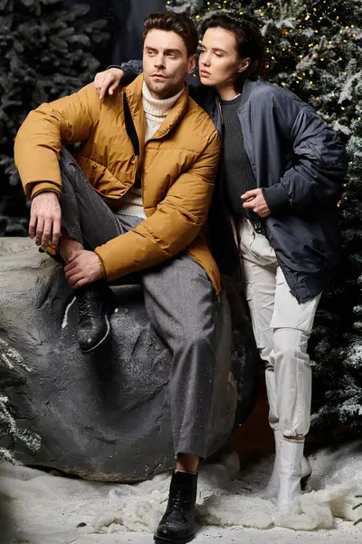 A couple enjoys a chilly day in warm jackets, sharing a loving moment among snow-laden pine trees. — Stock Photo