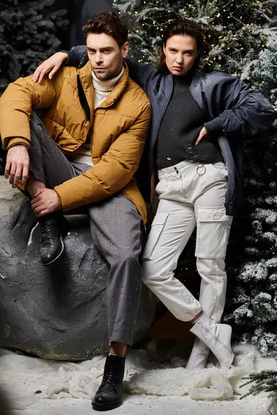 Un couple élégant habillé chaudement profite d'un paysage hivernal enneigé avec des pins majestueux, partageant une ambiance festive. — Photo de stock