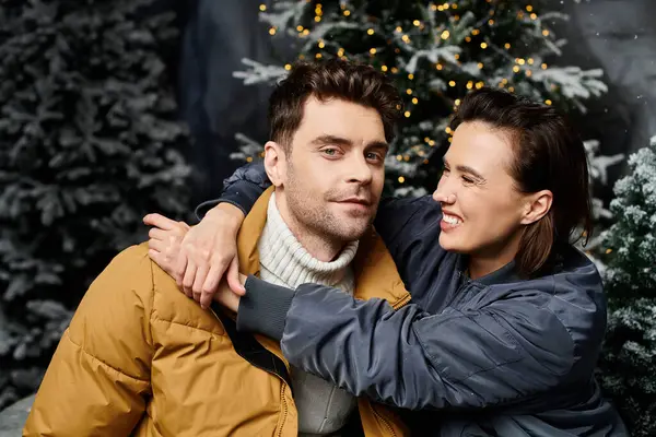 A couple dressed warmly shares a heartfelt moment near snow-draped pine trees, celebrating Christmas cheer. — Stock Photo