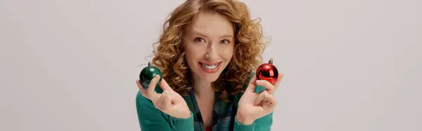 A cheerful young woman enjoys posing cheerfully while holding holiday ornaments in a bright setting. — Stock Photo