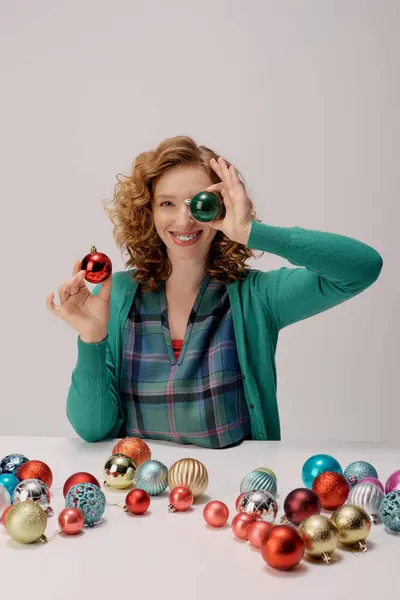 A cheerful young woman posing cheerfully surrounded by vibrant ornaments, embracing the holiday spirit. — Stock Photo