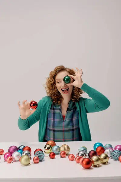 A cheerful young woman organizes vibrant ornaments while preparing for the holiday season. — Stock Photo