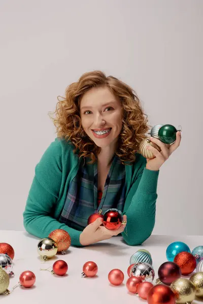 Uma jovem mulher com cabelo encaracolado alegremente mantém ornamentos coloridos enquanto se prepara para festividades. — Stock Photo