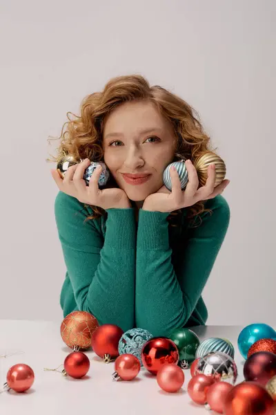 Smiling young woman holds colorful holiday ornaments, surrounded by vibrant decorations and cheer. — Stock Photo
