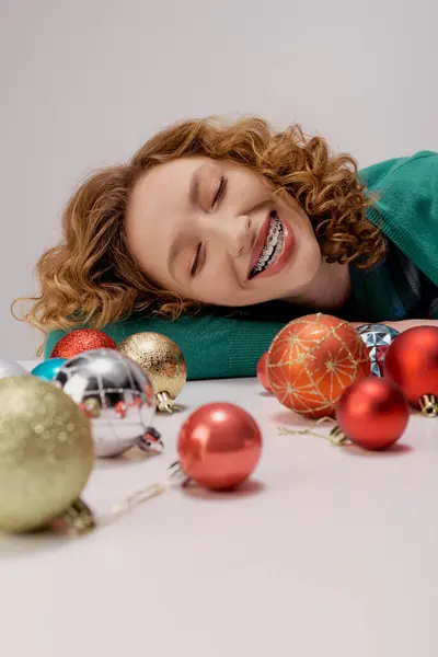 Eine fröhliche junge Frau posiert gern umgeben von glänzenden Ornamenten auf einem Tisch. — Stockfoto