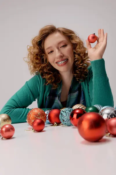A young woman with curly hair enjoys posing surrounded by vibrant holiday ornaments. — Stock Photo