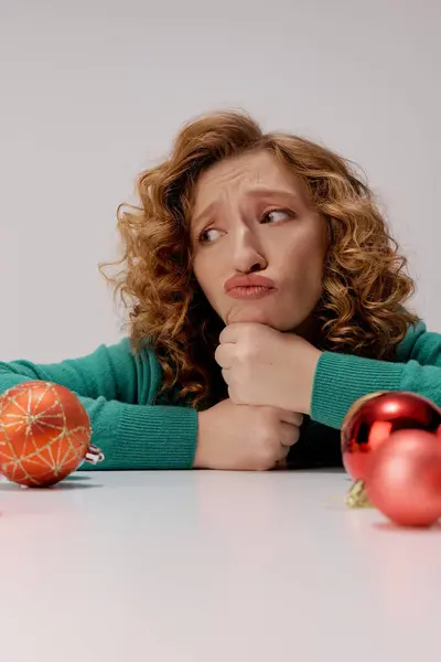 A young woman in green ponders while posing surrounded by ornaments and decorations. — Stock Photo