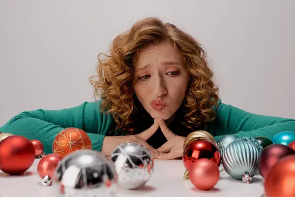 A young woman posing cheerfully at a table dotted with colorful holiday ornaments. — Stock Photo