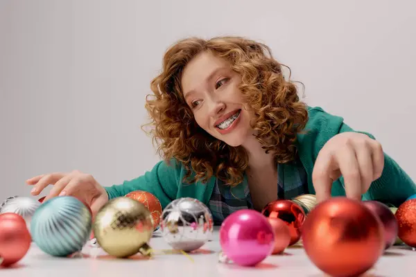 A cheerful young woman enjoys posing while playing with shiny ornaments around her. — Stock Photo