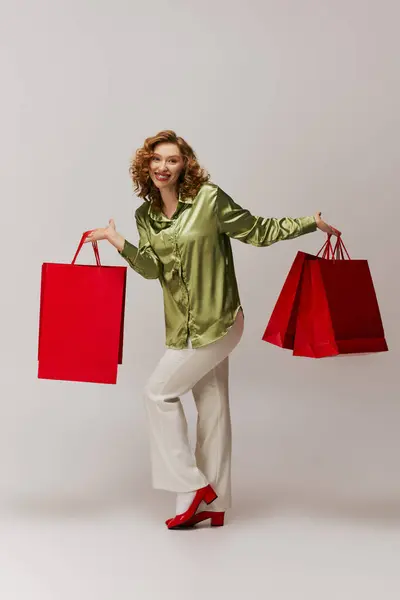 A cheerful young woman posing while excitedly holding red shopping bags. — Stock Photo