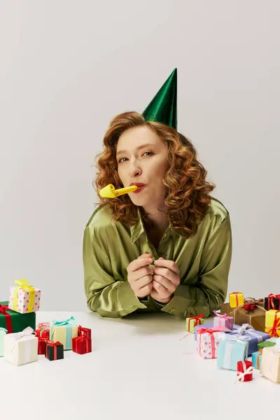 A young woman showcases her festive spirit while posing cheerfully, surrounded by colorful packages. — Stock Photo
