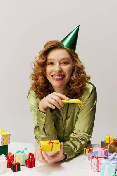 A young woman with curly hair is happily posing while wearing a party hat. — Stock Photo