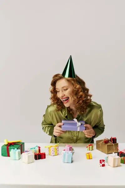 A young woman with curly hair smiles as she unwraps a beautifully wrapped gift surrounded by others. — Stock Photo